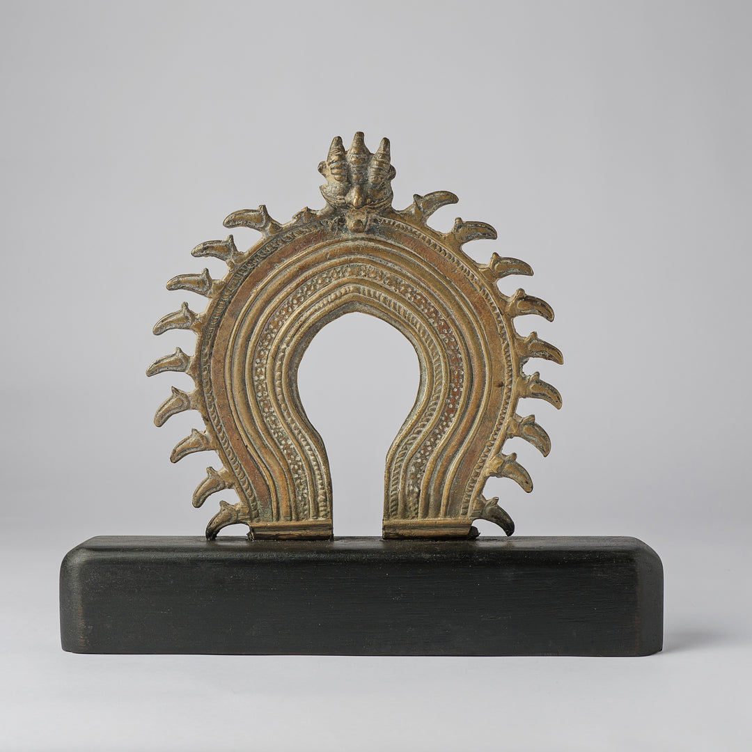 Decorative metal object with intricate design on a black base against a gray background