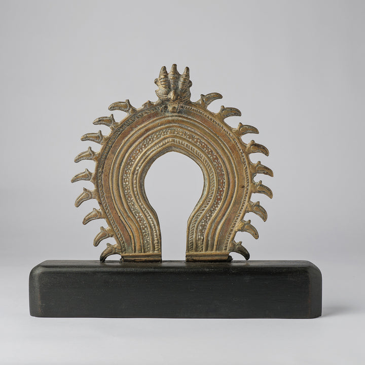 Decorative metal object with intricate design on a black base against a gray background
